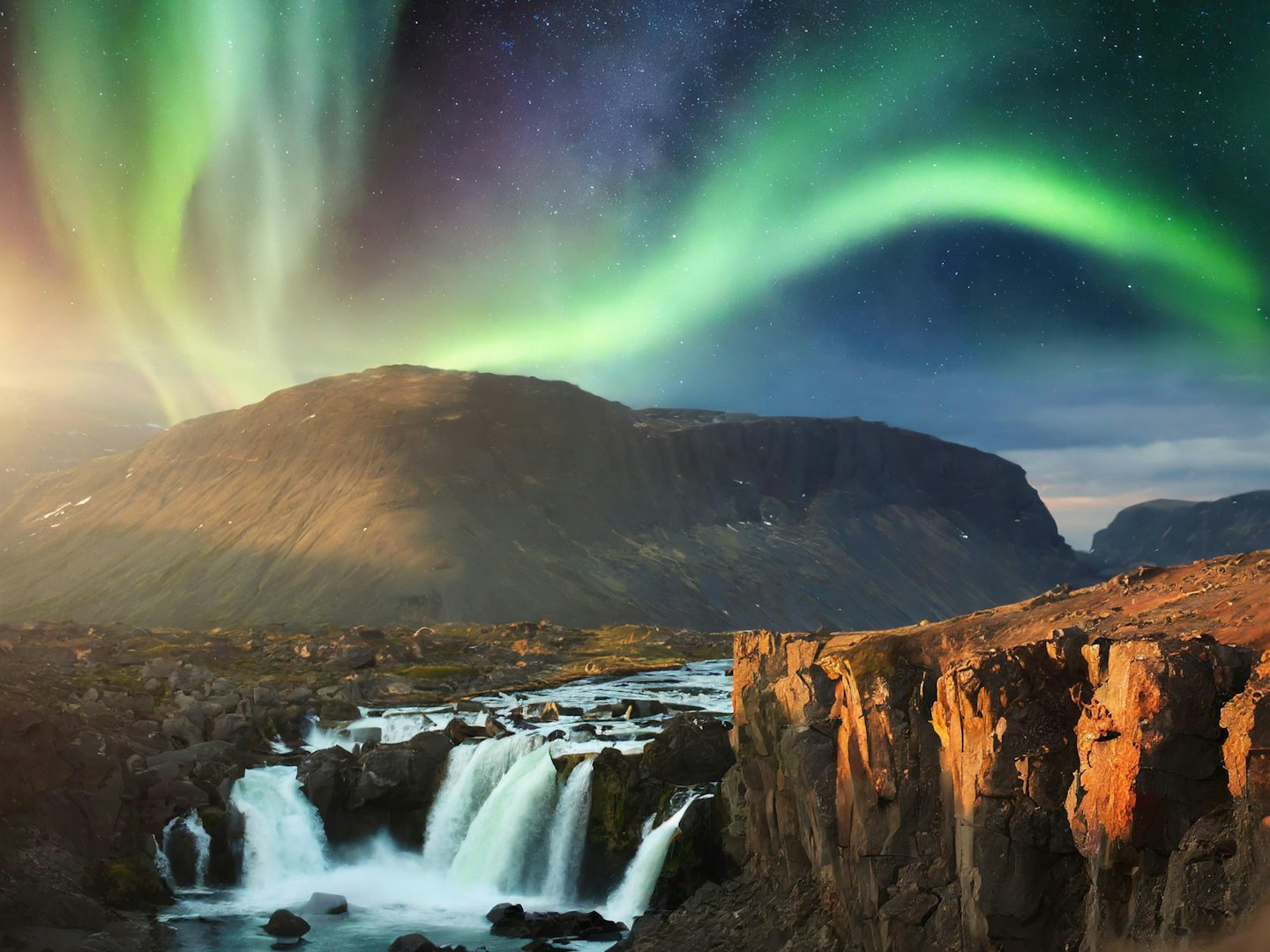 Waterfall cascades over rocks under Northern Lights.