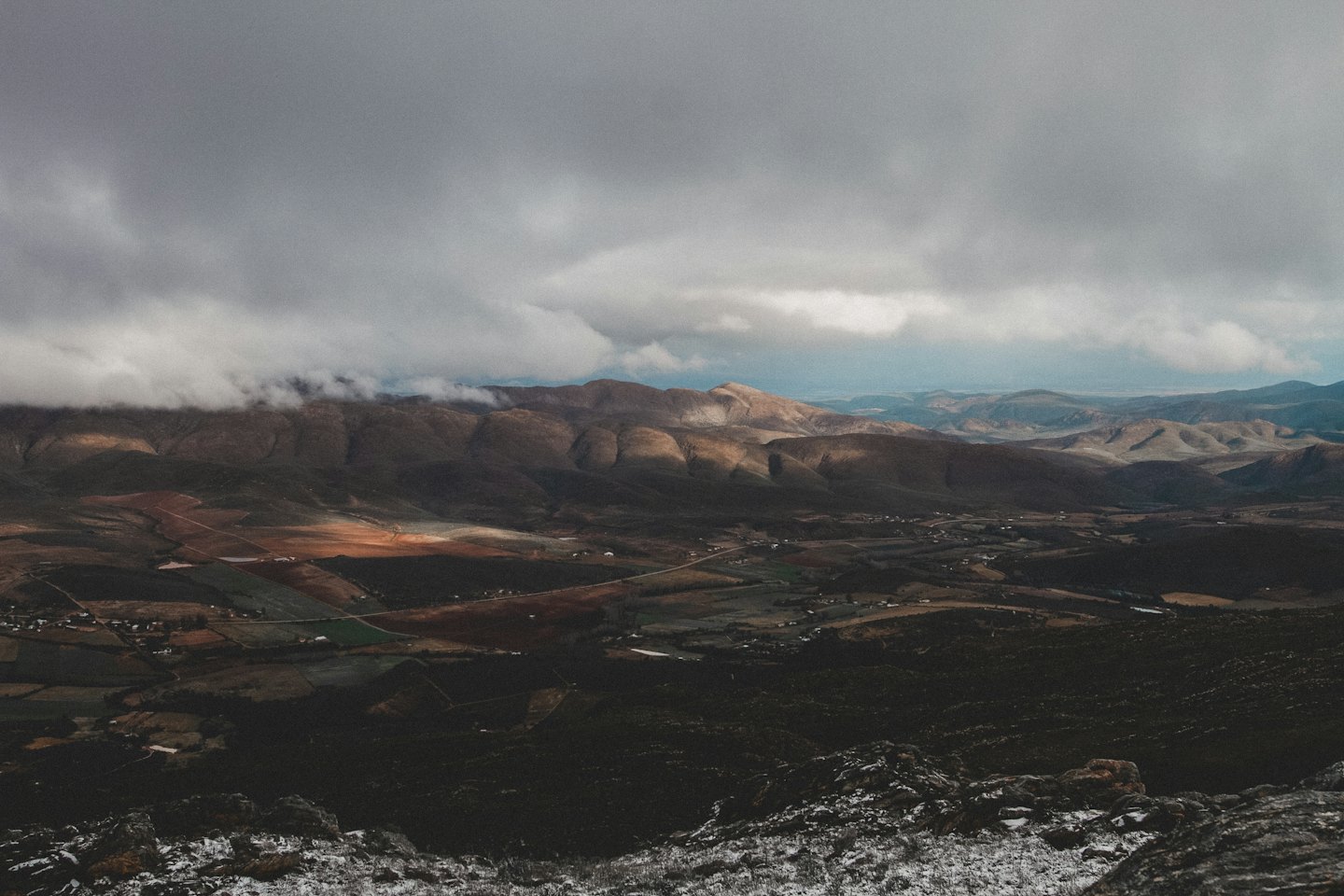 Sunlit rolling hills and cultivated fields under cloudy sky.