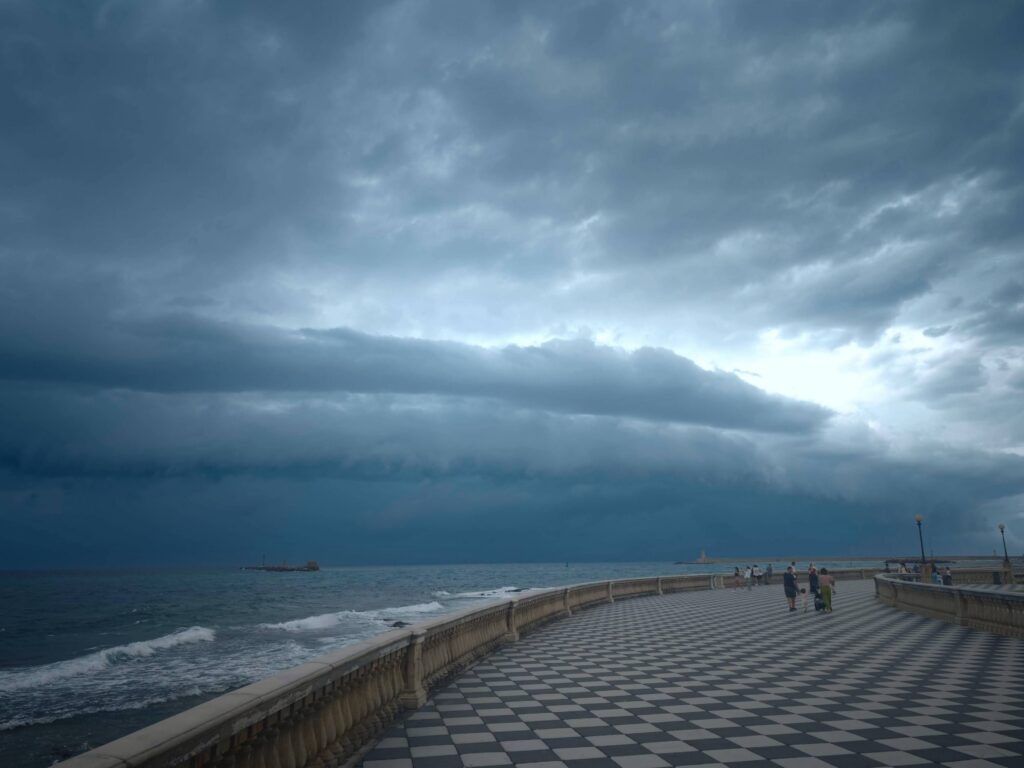 Curved seafront promenade with black-and-white checkered pavement beneath layered storm clouds.
