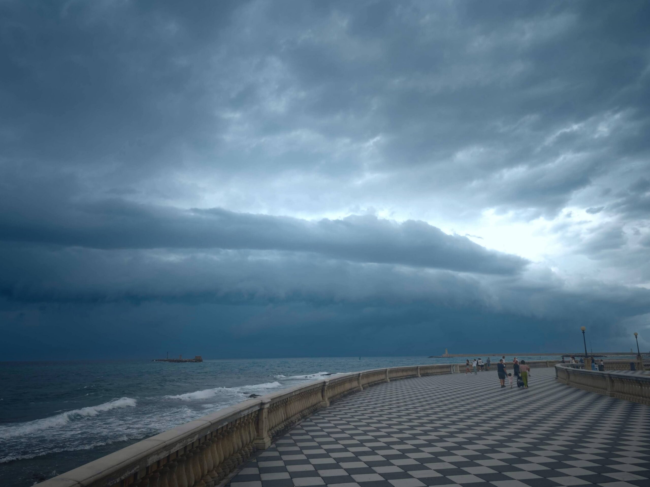 Curved seafront promenade with black-and-white checkered pavement beneath layered storm clouds.