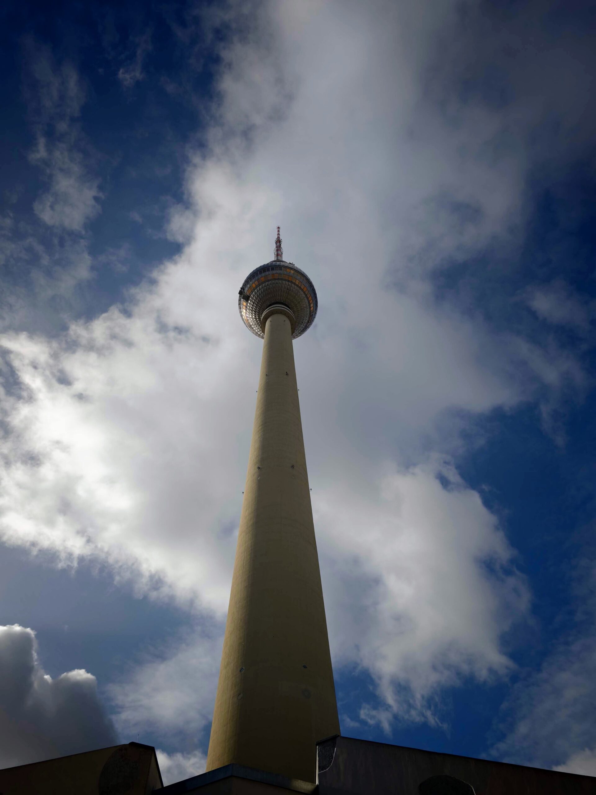 Low-angle photo of a tall broadcast tower with a round observation sphere against cloudy blue sky.