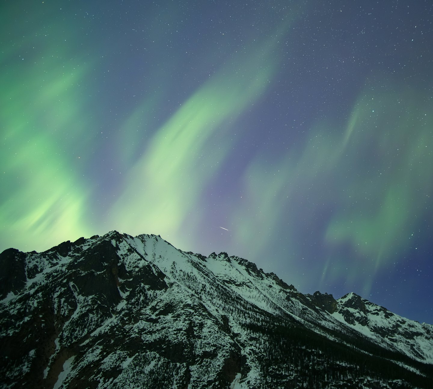 Green aurora borealis shines above the snow-covered mountain peaks.
