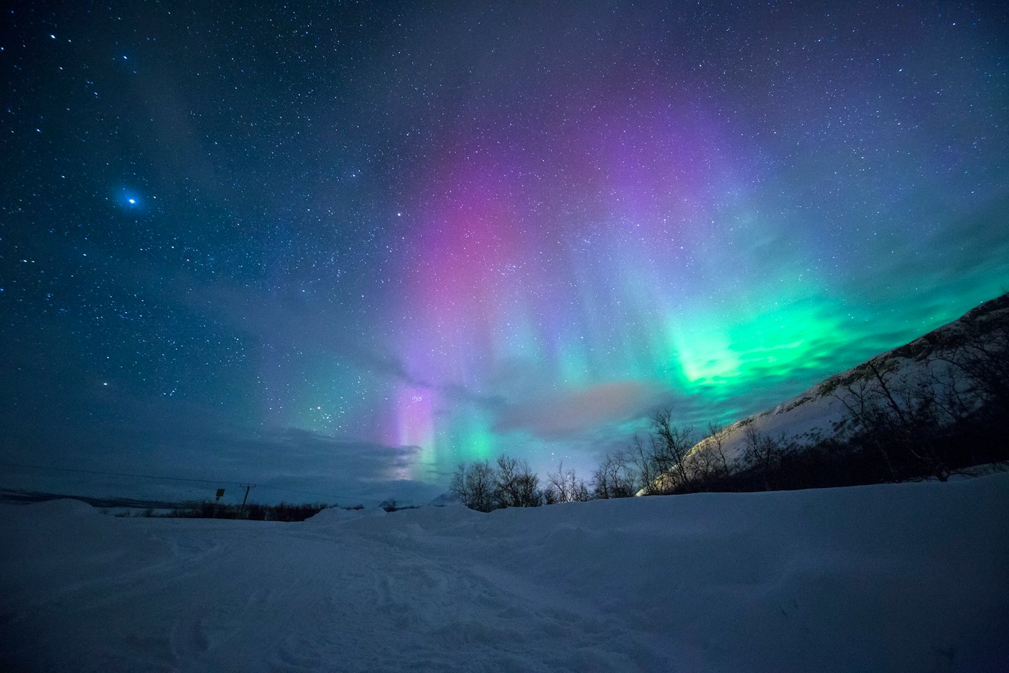 Aurora borealis shines brightly over a snowy landscape.