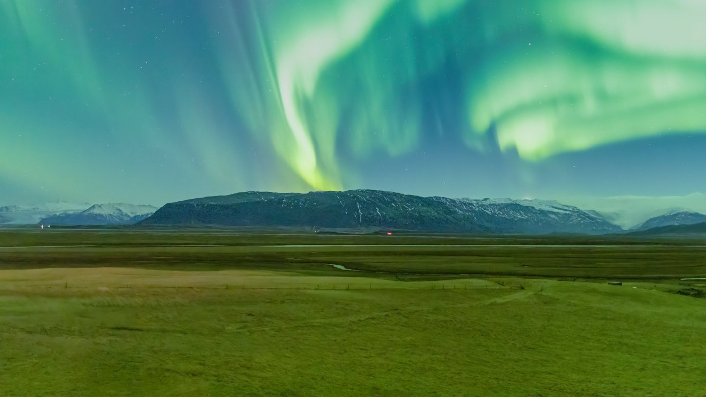 Northern lights shine above a river and mountain landscape.