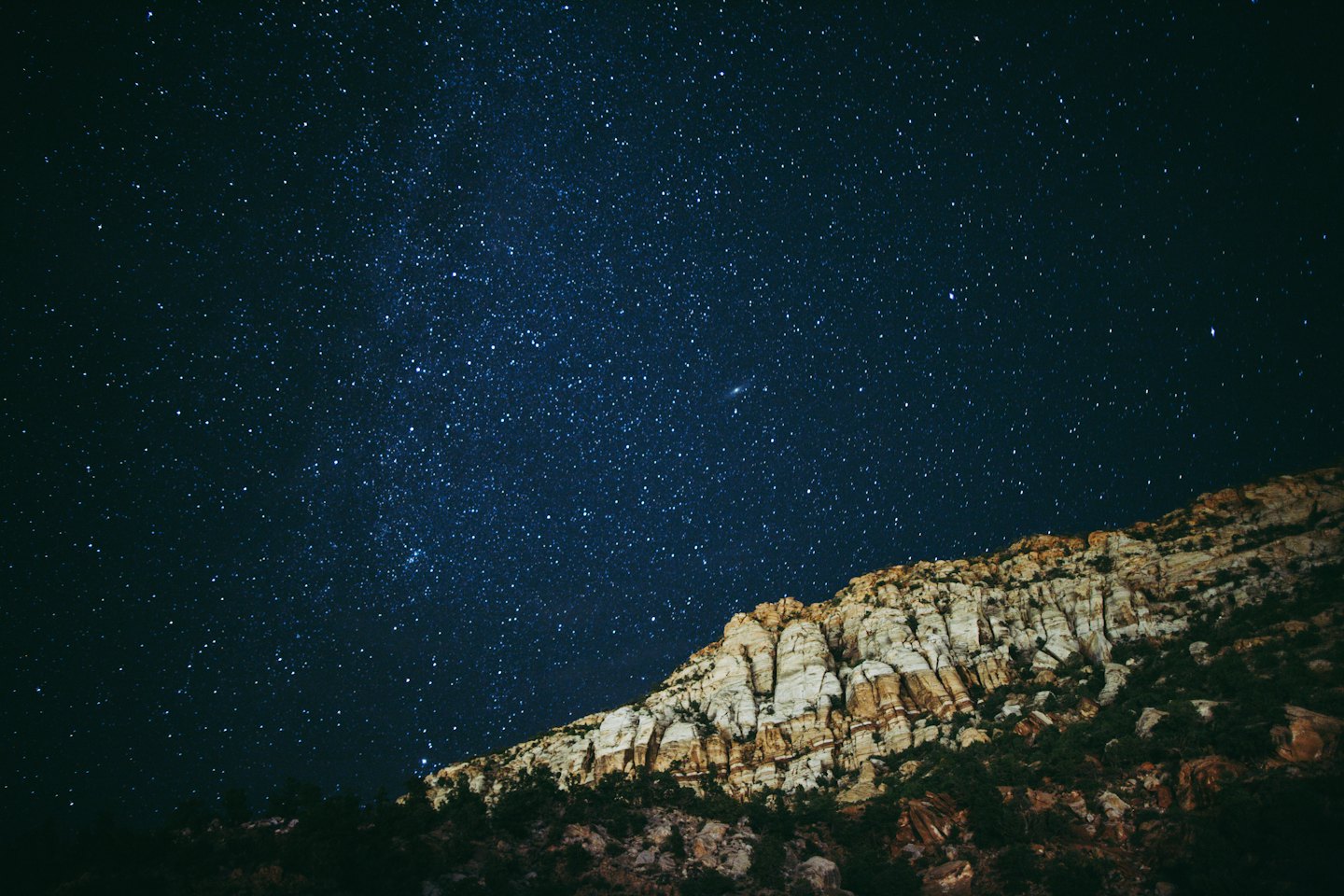 Stars fill the night sky above a rocky mountain range.